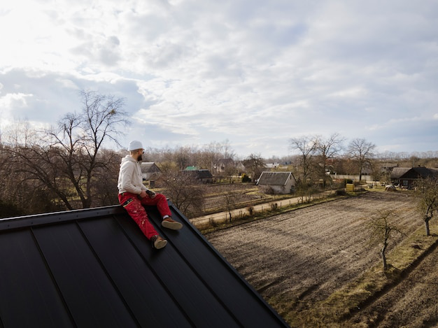 A person with a helmet sitting on a roof Hire the best roof cleaners in Boynton Beach