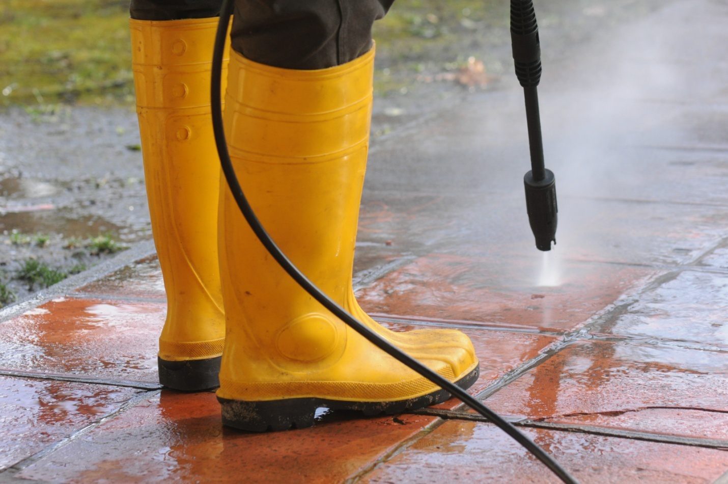 A person wearing yellow boots cleaning a home's exterior